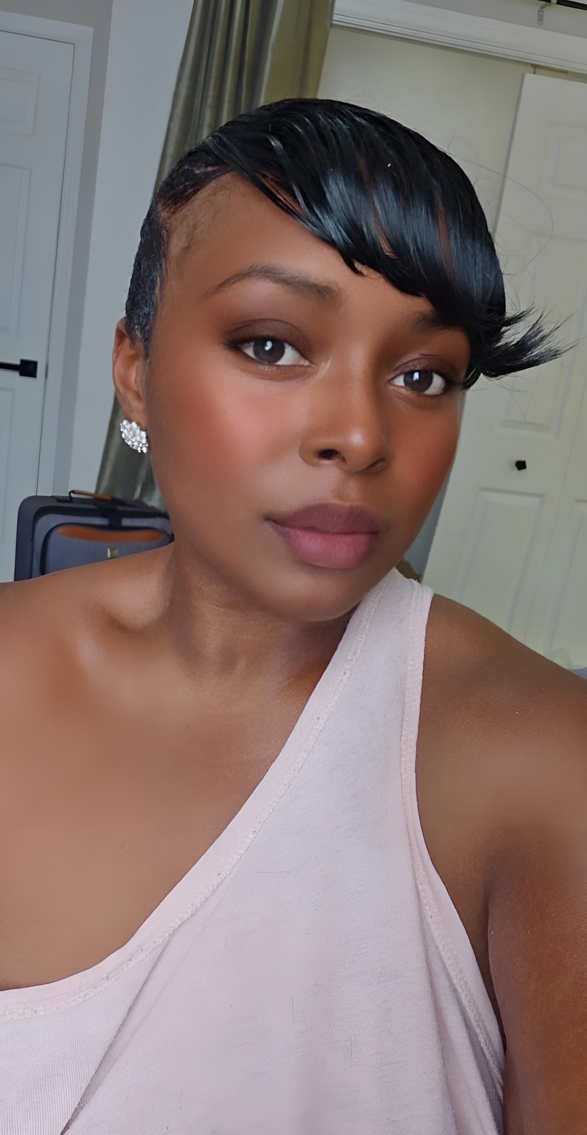 Black woman with short black hair and side-swept bangs wearing a pink one-shoulder top.