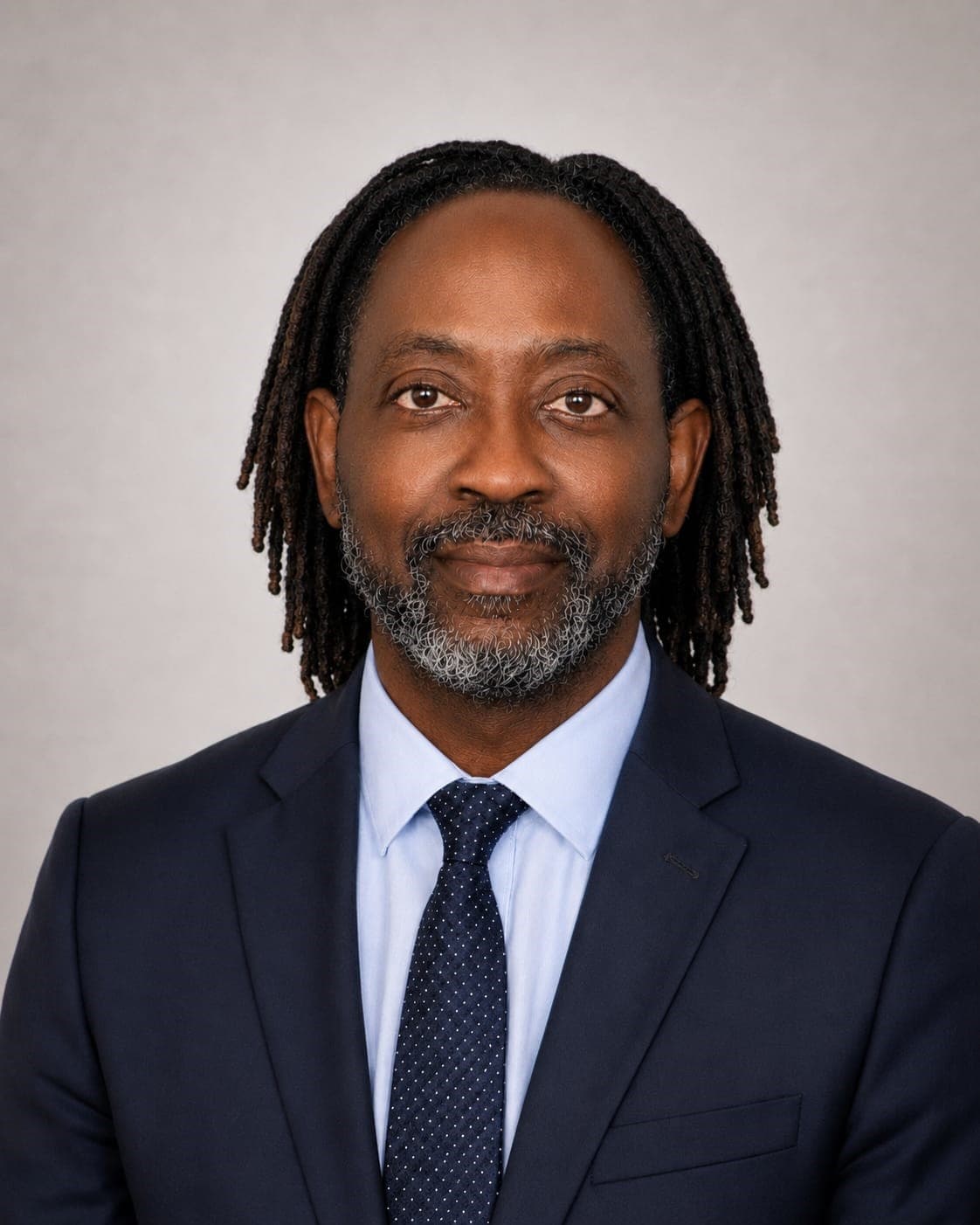Black man with dreadlocks and a salt-and-pepper beard wearing a navy suit and blue tie.